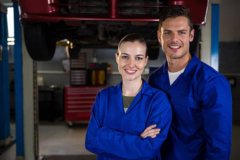Due meccanici sorridenti in tuta blu, officina.